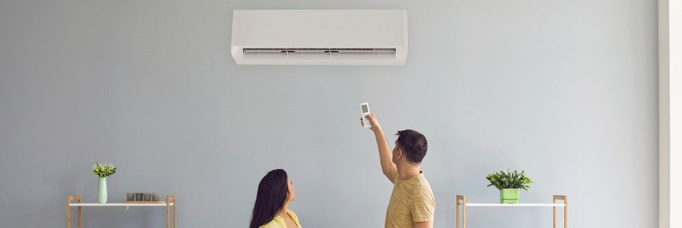 A person operating an air conditioner with a remote, another person is nearby.