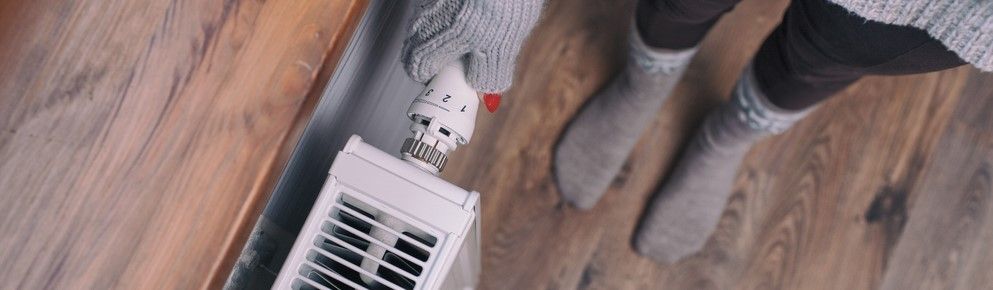 Person wearing grey socks and sweater, standing near a radiator on a wooden floor.