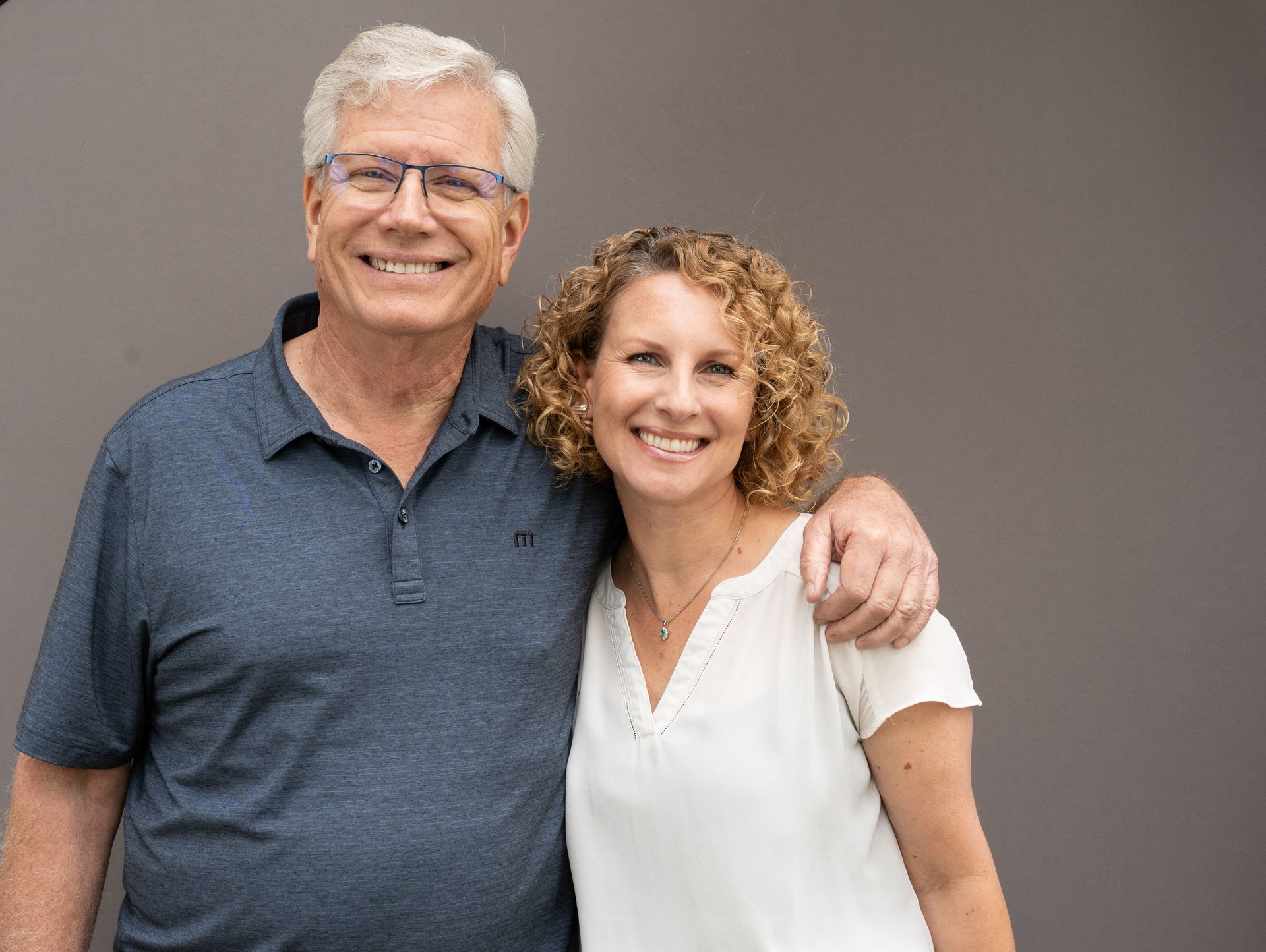 Bruce and Margie smiling with arms around each other against a gray background. | Westlake Independent Automotive