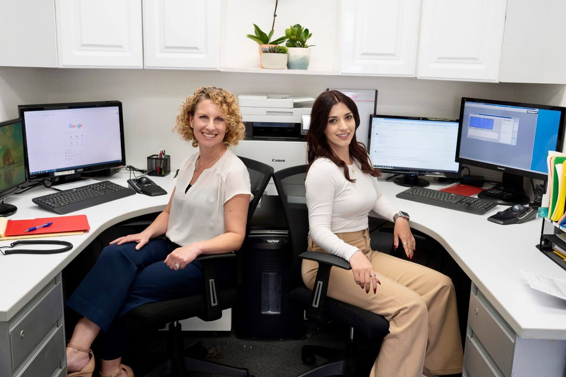 Two people seated at a shared office workstation with multiple computer monitors and keyboards | Westlake Independent Automotive