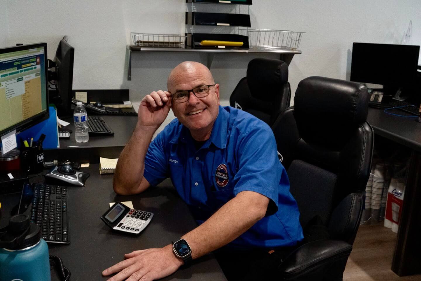 Man smiling at a desk in an office, wearing a blue shirt and headset, with computer monitors nearby | Westlake Independent Automotive