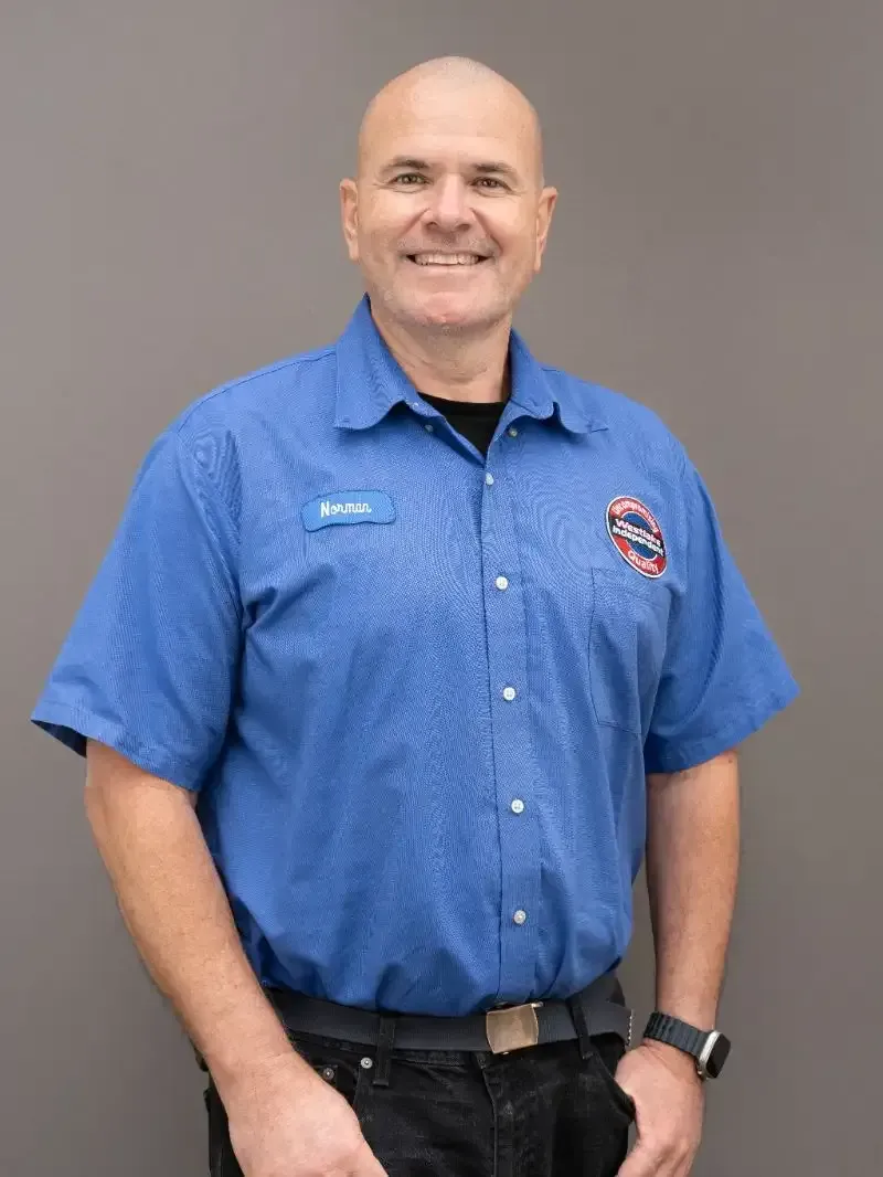 Smiling man in blue button-up shirt and black pants standing against a plain gray background. | Westlake Independent Automotive