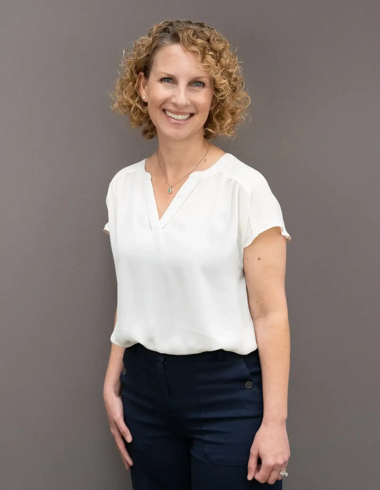 Smiling person in white blouse and dark pants standing against a gray background | Westlake Independent Automotive