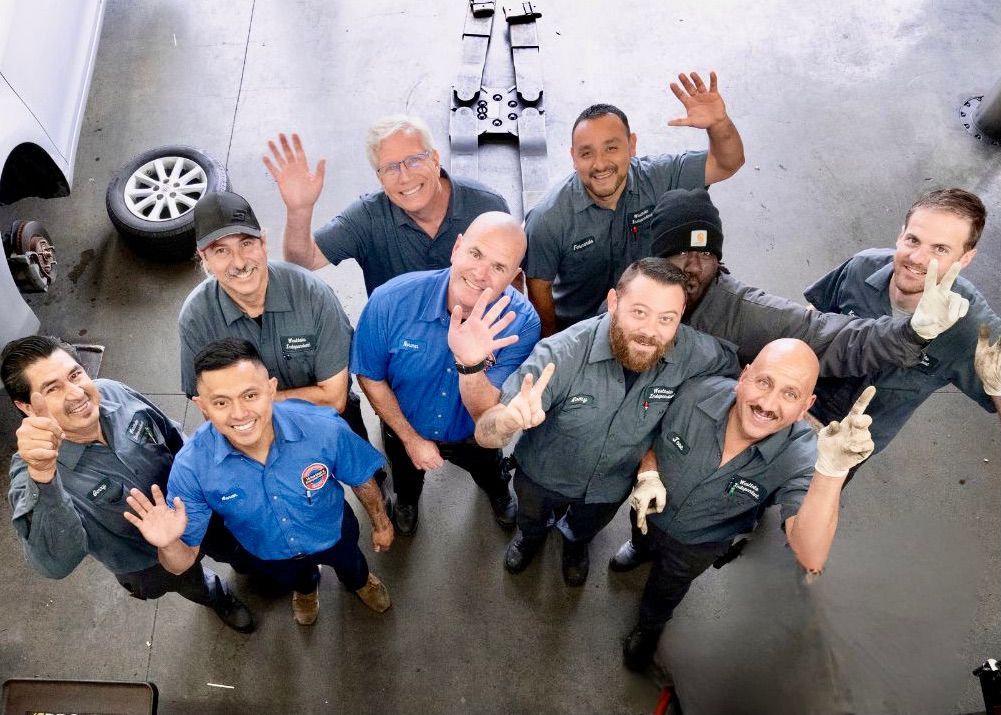 Group of uniformed workers smiling and waving up at the camera in an industrial setting | Westlake Independent Automotive