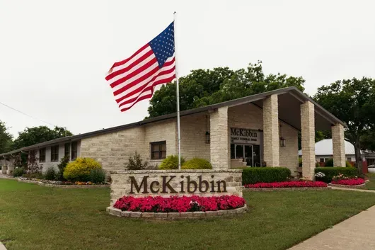 McKibbin Funeral Home with a large American flag and landscaped flower beds on a clear day