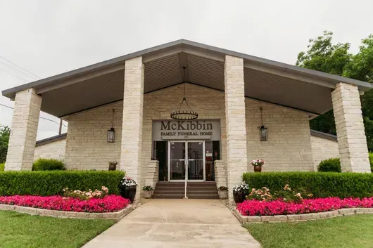 McKibbin Funeral Home entrance with steps, glass doors, and pink flower beds along the walkway