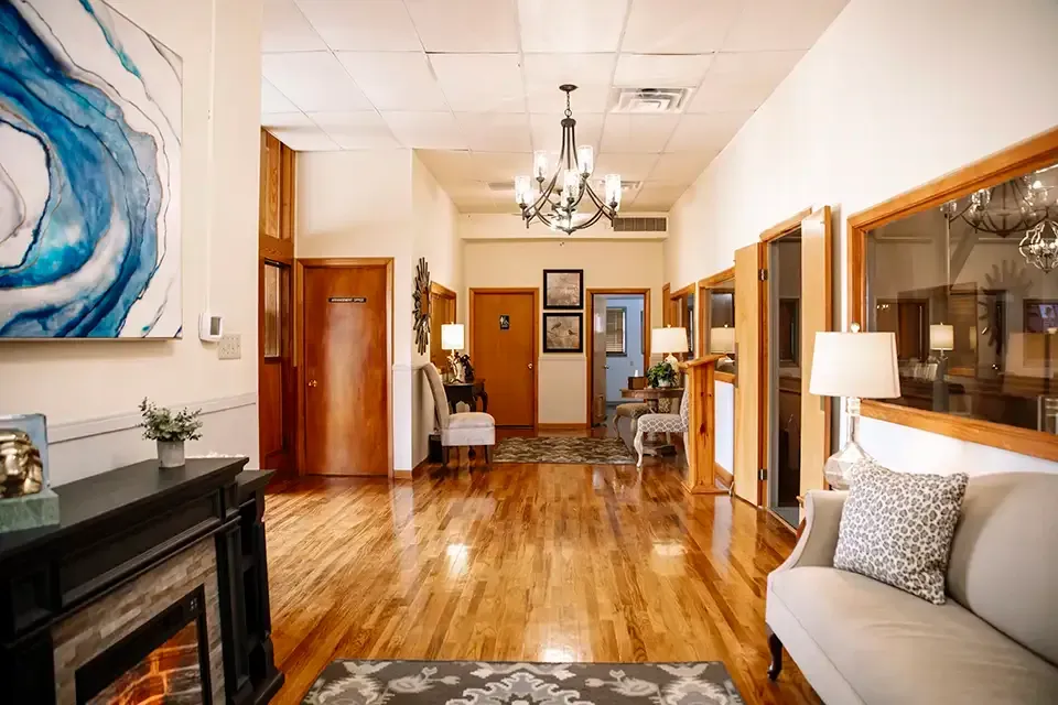 Elegant hallway with hardwood floors, chandelier, fireplace, and framed artwork in a warmly lit interior