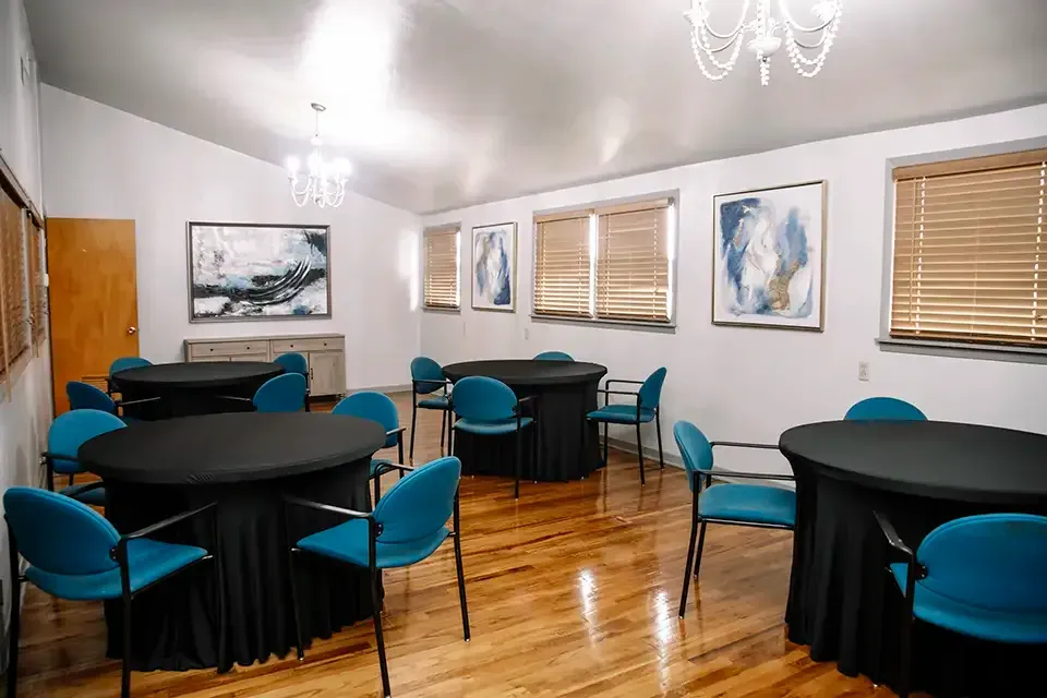 Small banquet room with round black tables, teal chairs, wood floors, and framed art on the walls