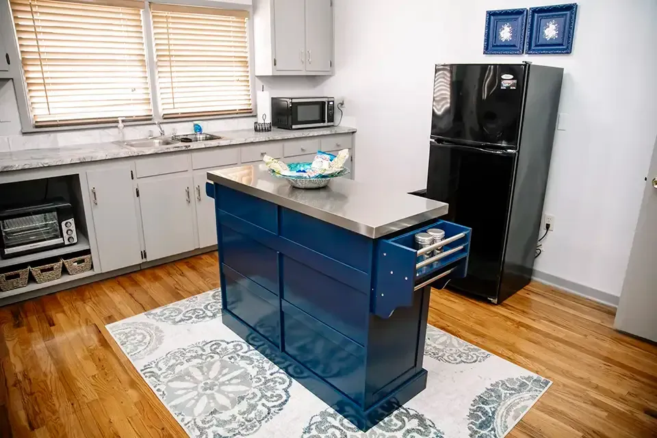 Modern kitchen area with blue island, black refrigerator, white cabinets, and hardwood floor