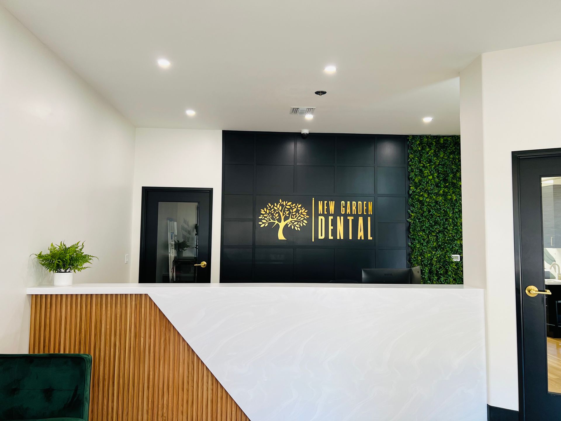 Reception desk in a dental office; black accent wall with gold logo, white and wood-toned desk.