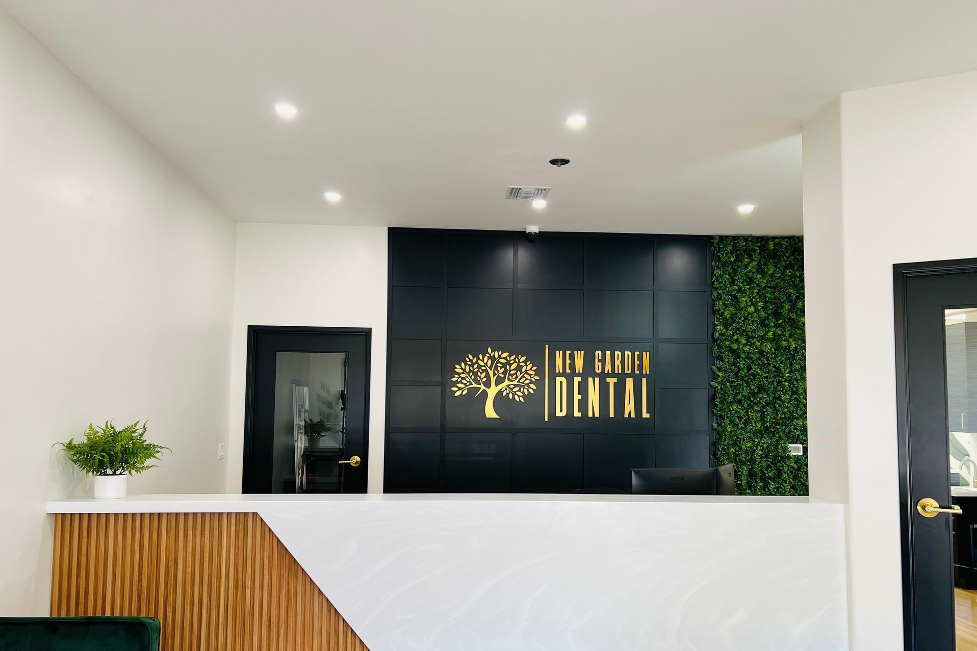 Dental office reception area with a white and wood grain counter, black paneling, and a green wall.