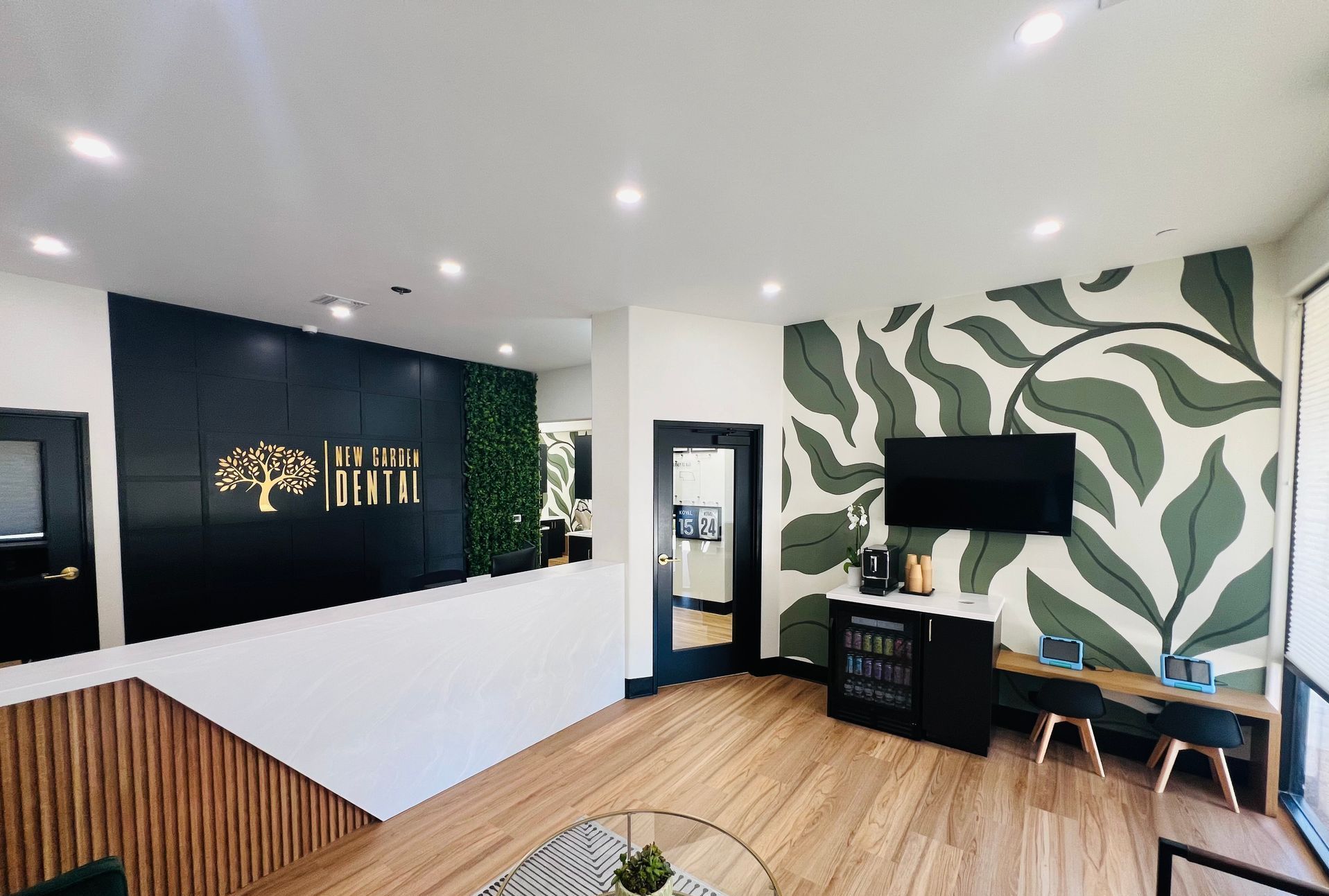 Lobby with leaf mural, dark accent wall, gold logo, and waiting area with TV and refreshments.