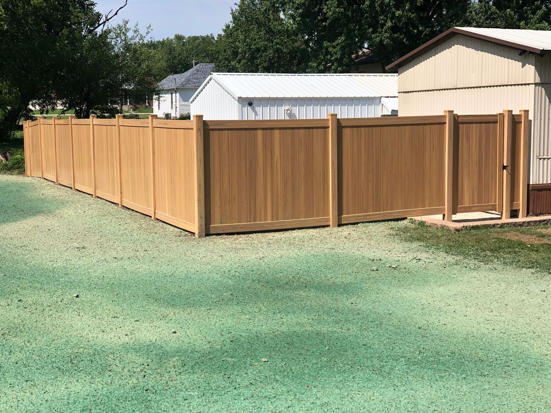 A wooden privacy fence surrounds a gravel yard with a shed in the background.