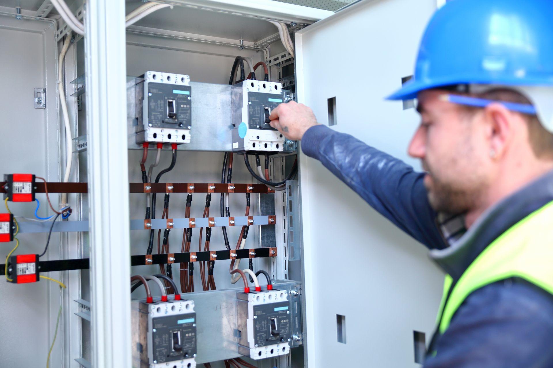 A man in a blue hard hat is working on an electrical box.