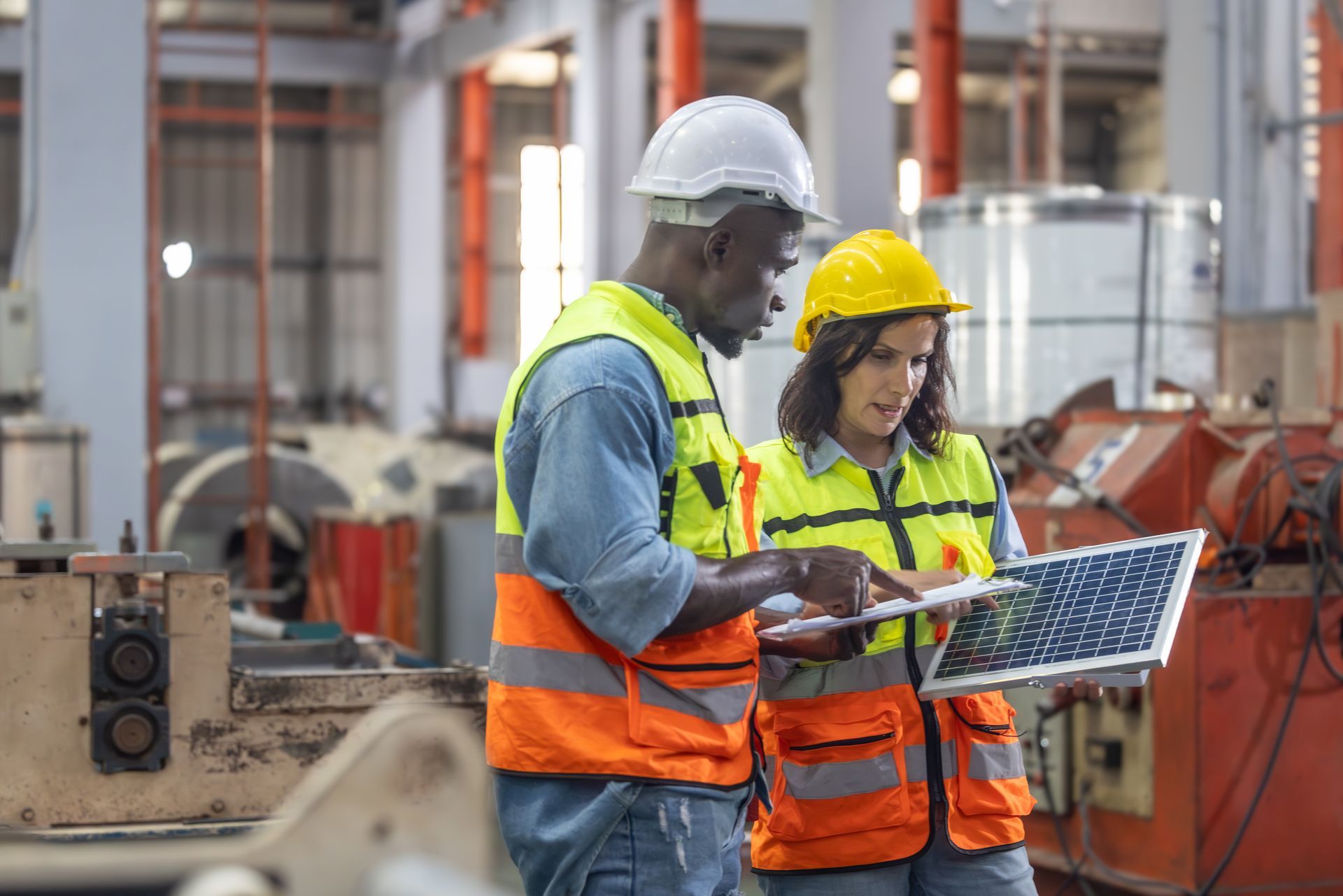 A man and a woman are looking at a laptop in a factory.