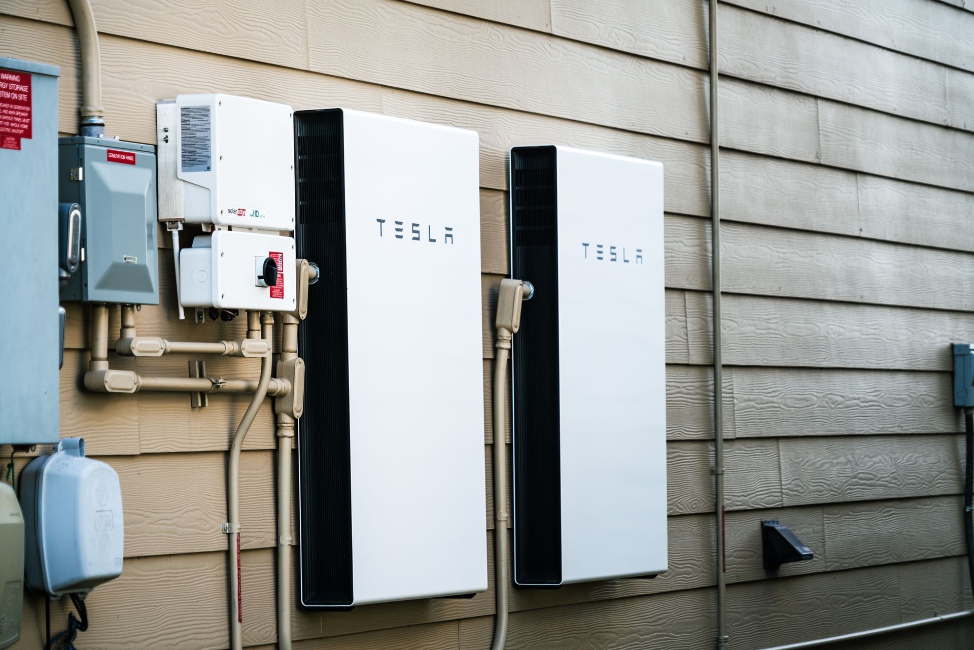 Two tesla batteries are installed on the side of a house.