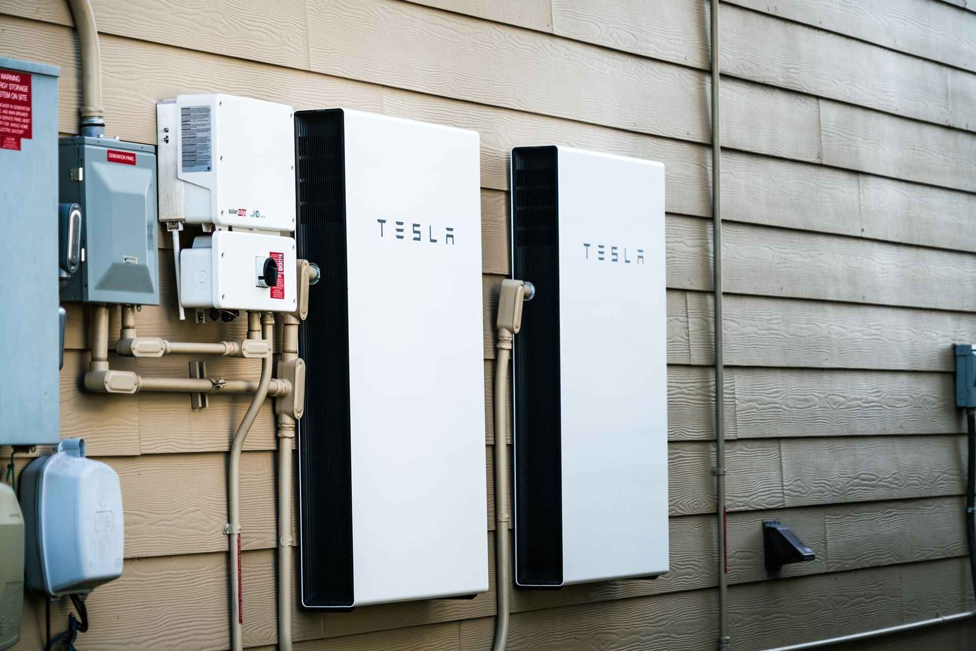 Two tesla batteries are mounted on the side of a house.