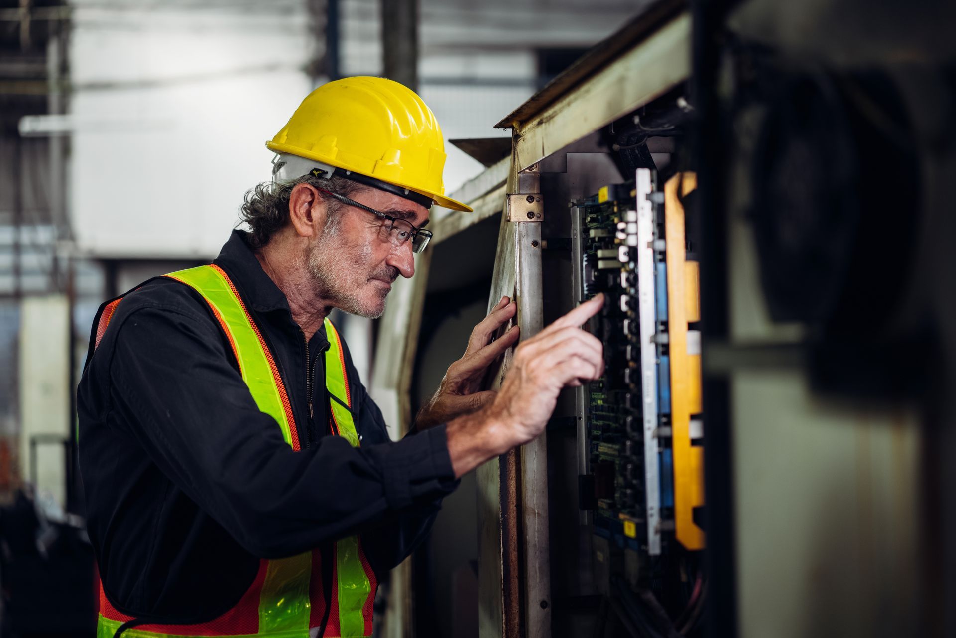 A man wearing a hard hat and safety vest is working on a machine in a factory.