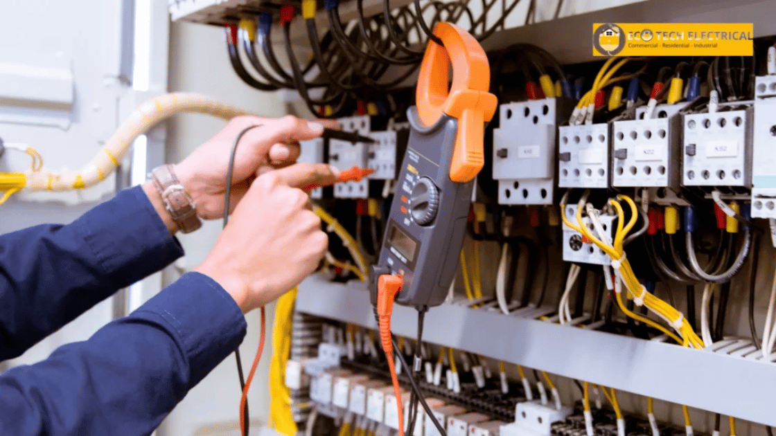 Electrician using a clamp meter to measure current in an electrical panel with various wires and components.