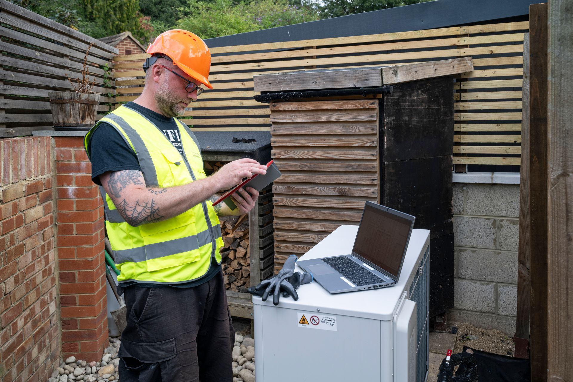 A man wearing a hard hat and safety vest is standing next to a laptop computer.