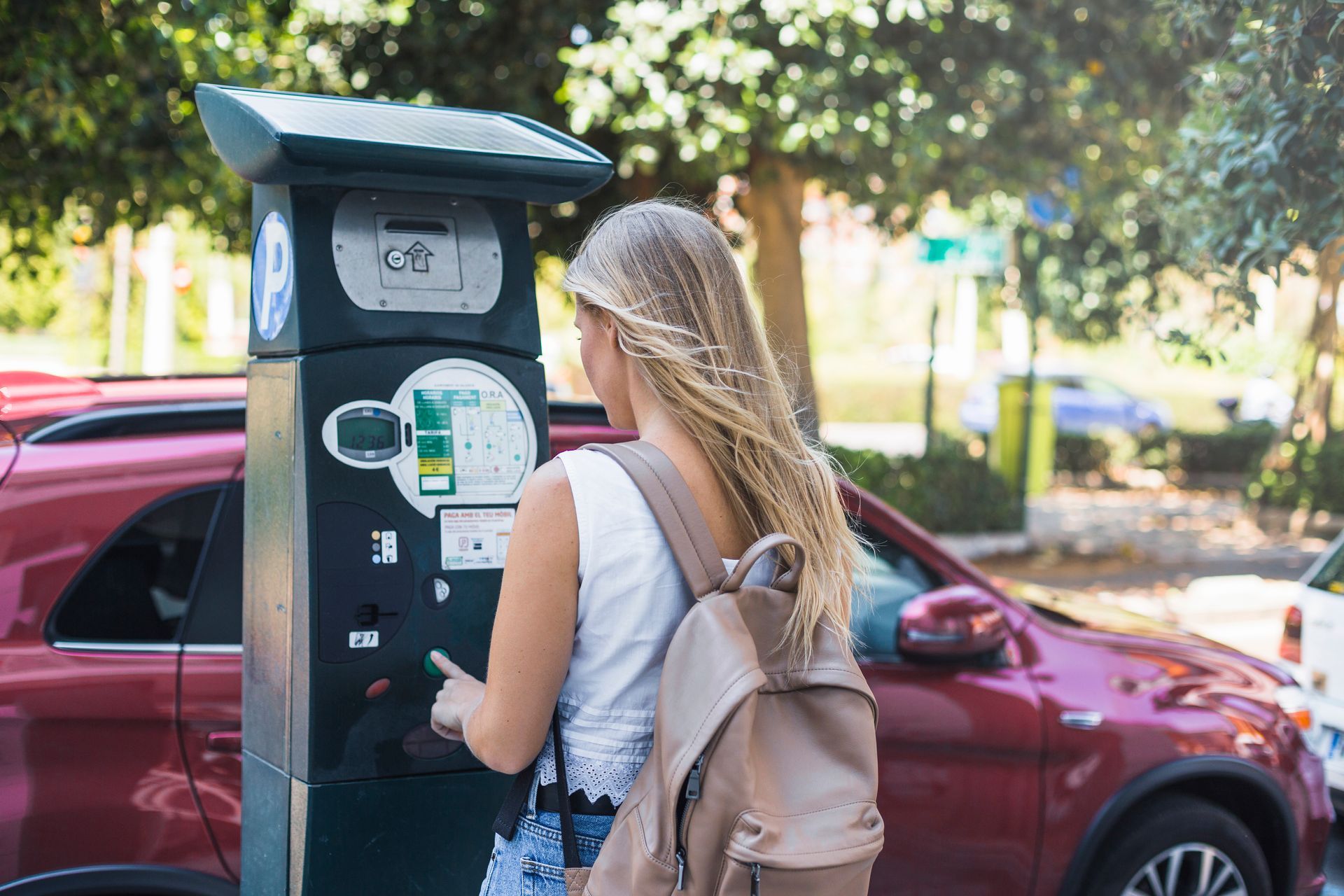 A woman is standing in front of a parking meter.