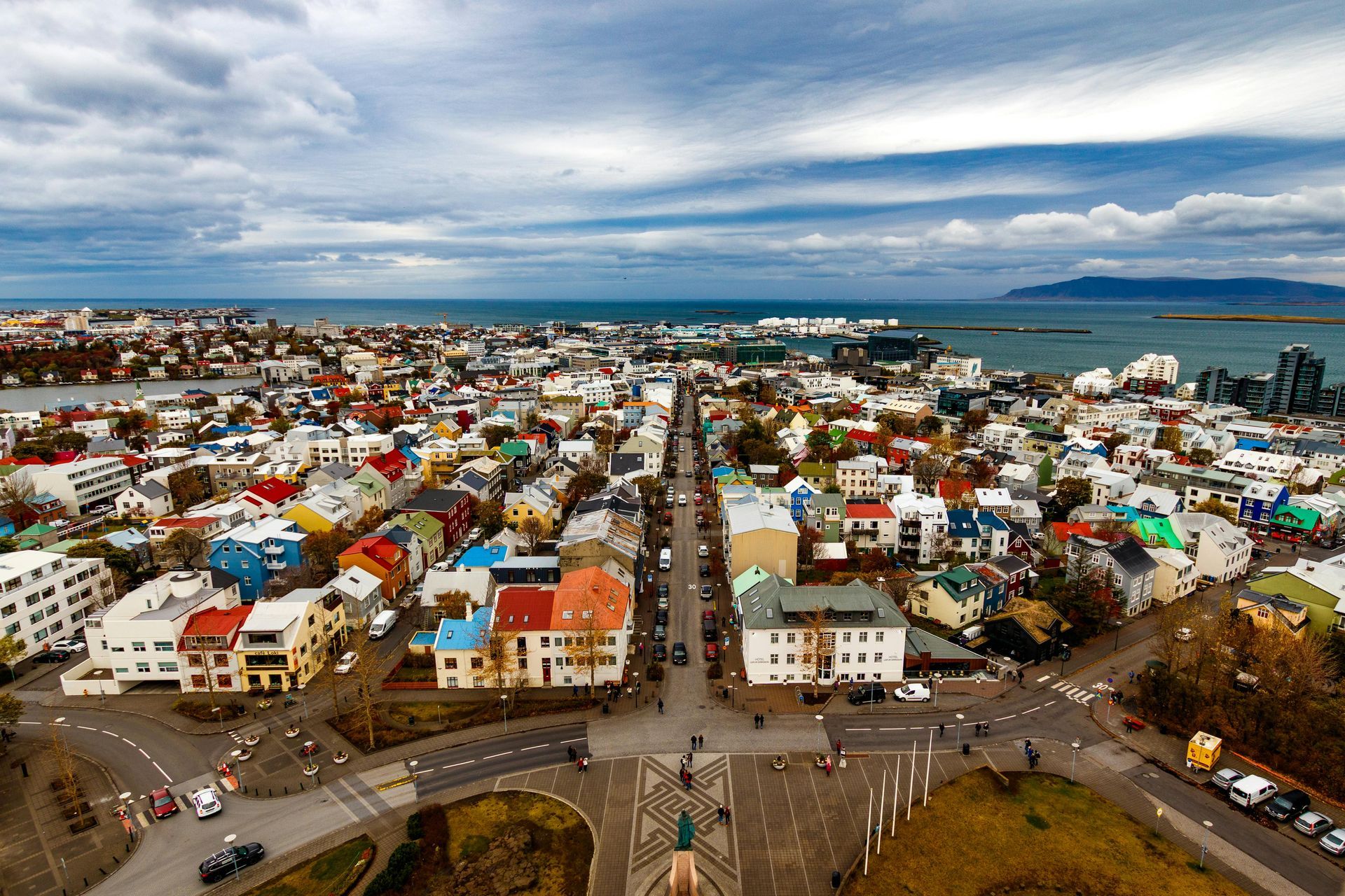 Aerial view of Reykjavik, Iceland, with colorful buildings, roads, and the ocean under a cloudy sky.