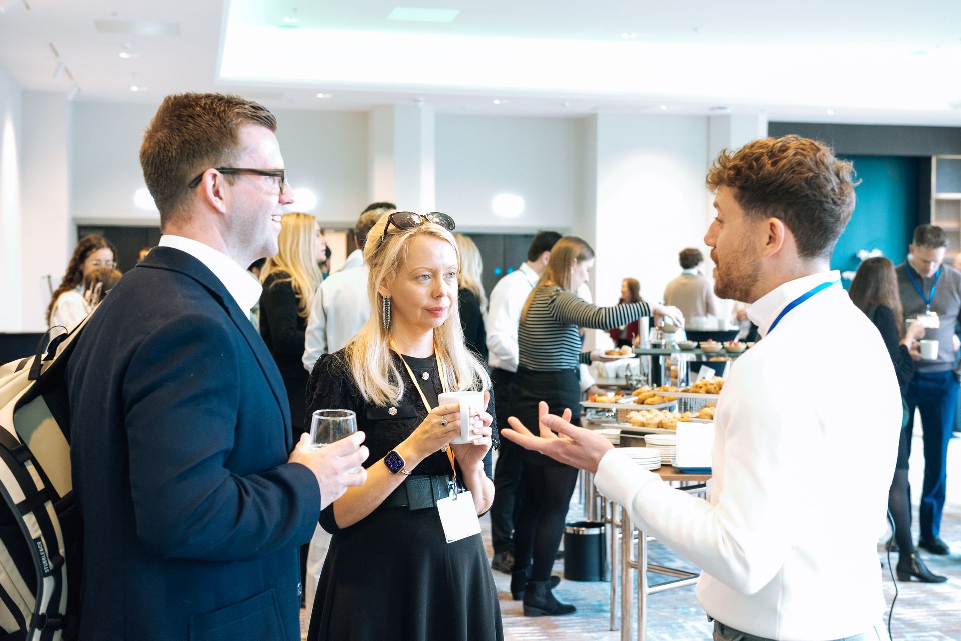 People networking at a conference, holding drinks and talking in a bright event space