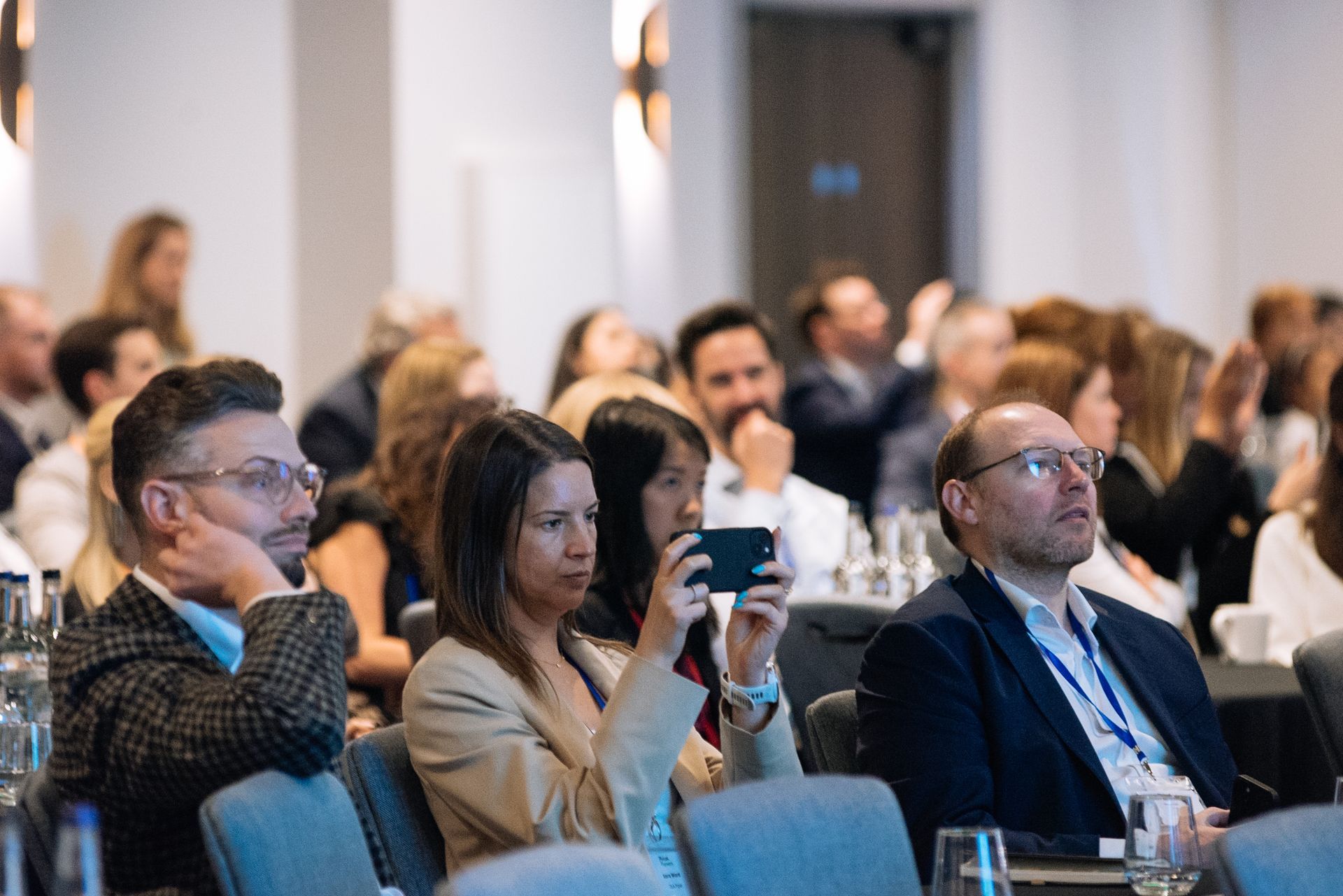 Audience seated at a conference, with one person holding up a phone to take a photo