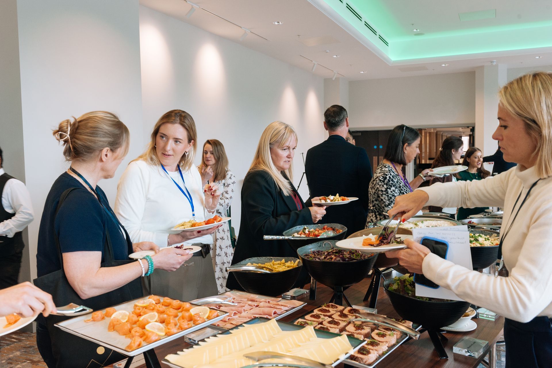 People serving and selecting food at a buffet table in a bright conference room