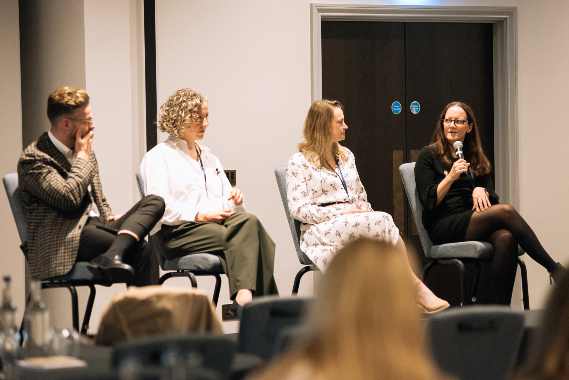 Panel discussion with four seated speakers in a conference room; one woman speaks into a microphone.