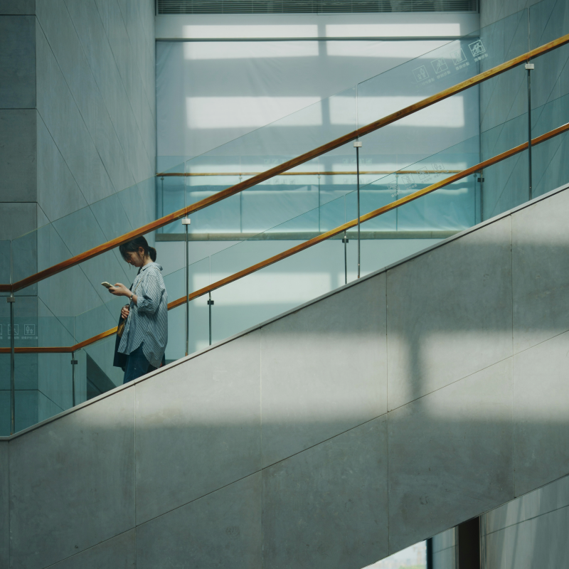 Person reading on a stairway in a bright modern interior with glass railings
