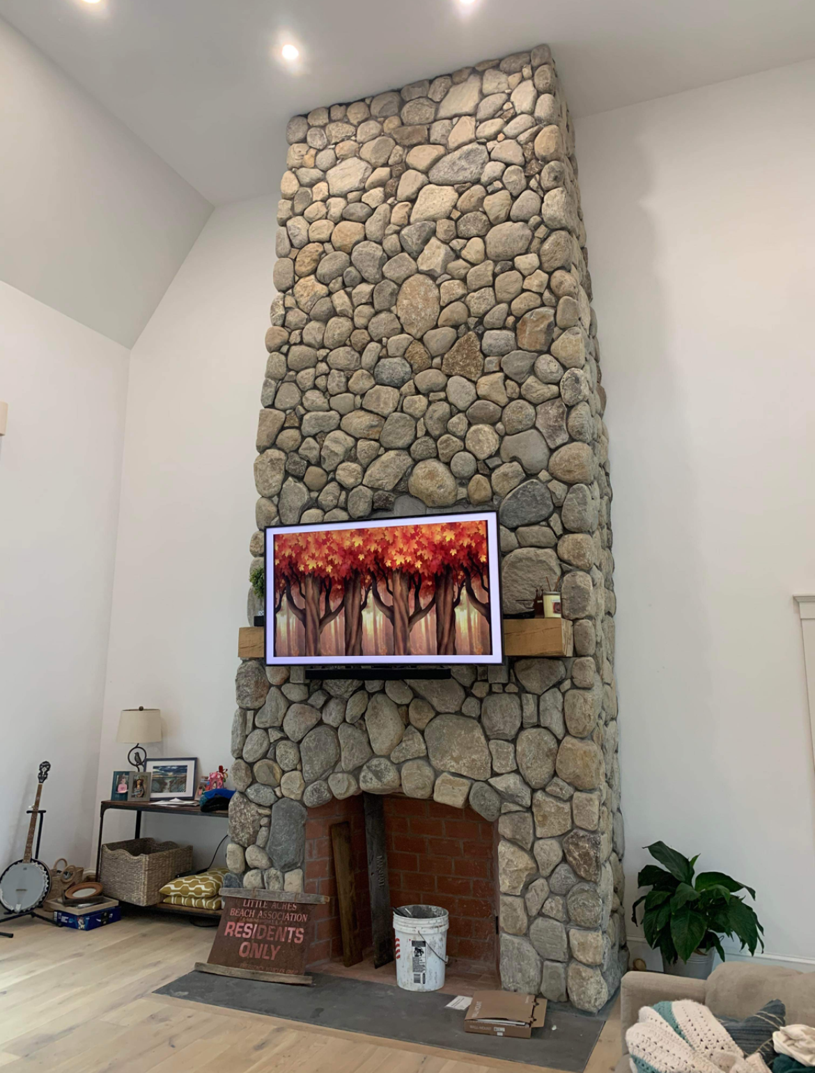 A tall, floor-to-ceiling river rock fireplace in a light-walled room, featuring a television mounted above the hearth.
