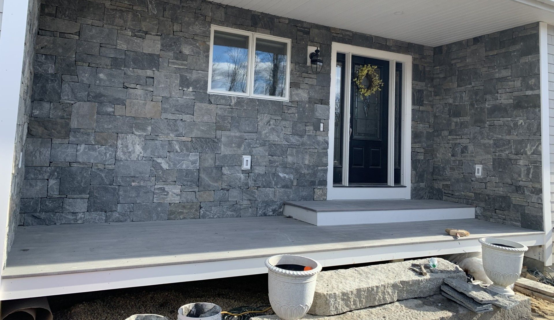 A house entryway featuring a gray stone facade, a dark front door, a white-framed window, and a gray concrete porch.