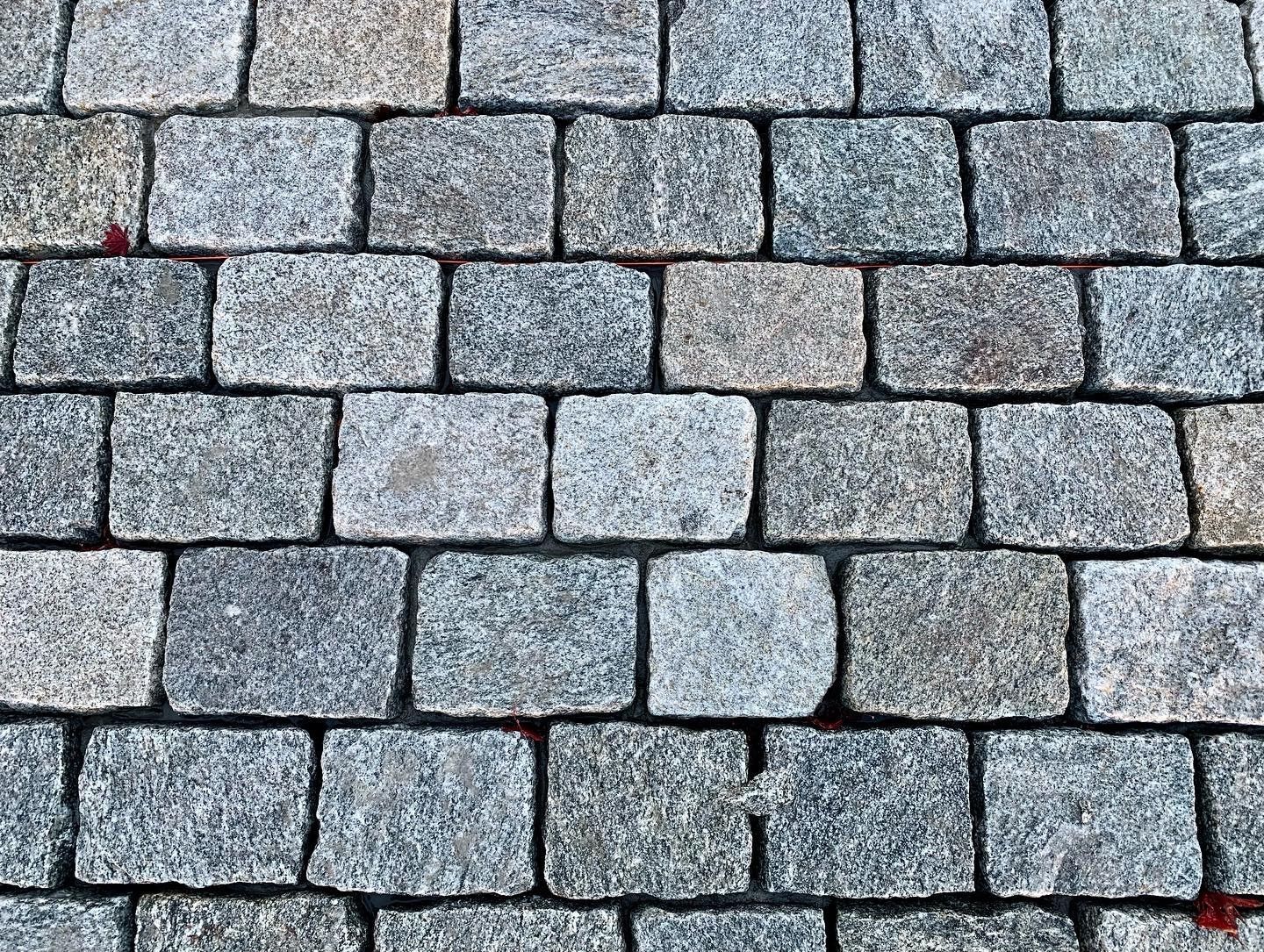 A close-up view of textured, grey granite paving stones arranged in a uniform grid pattern on the ground.
