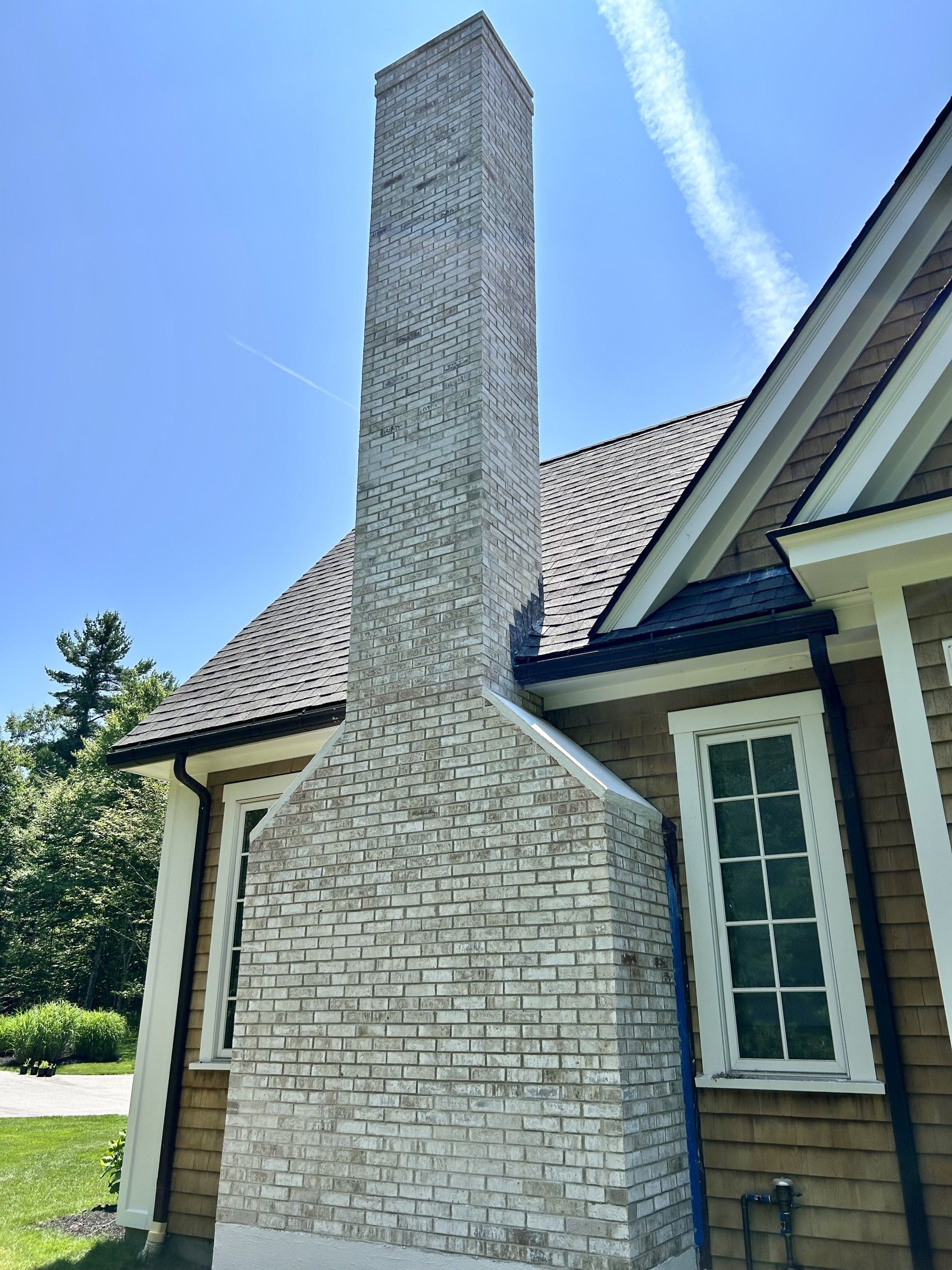 A tall, light-colored brick chimney rises against the side of a brown house under a bright blue sky.