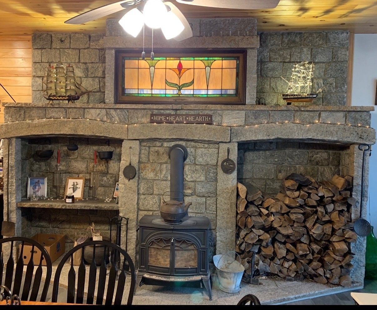 A large stone fireplace wall featuring a central wood stove, a stained-glass window above it, and an integrated log storage.