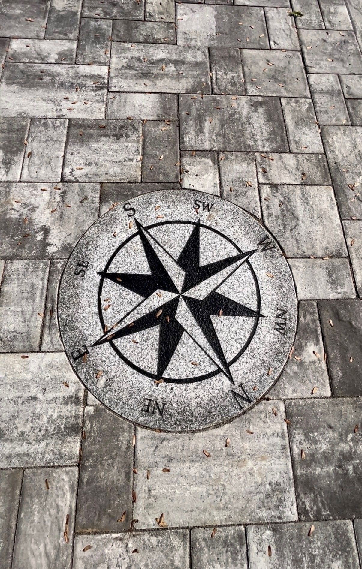 A circular compass rose design inlaid into a gray stone paver patio.