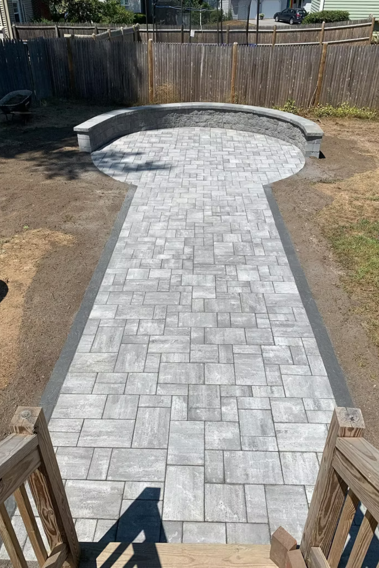 A stone paver walkway leading to a circular seating area with a curved stone retaining wall in a grassy backyard.