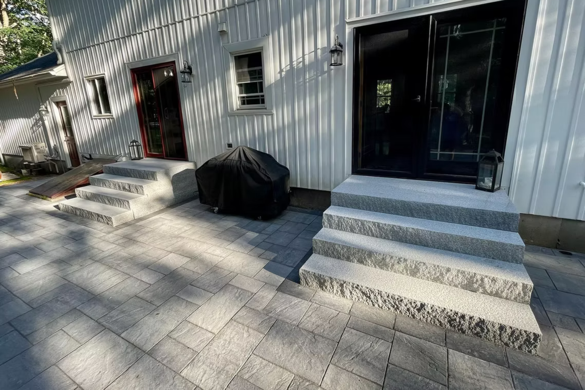 Exterior view of a home with light grey stone steps leading to two doorways, set against a grey paver patio.