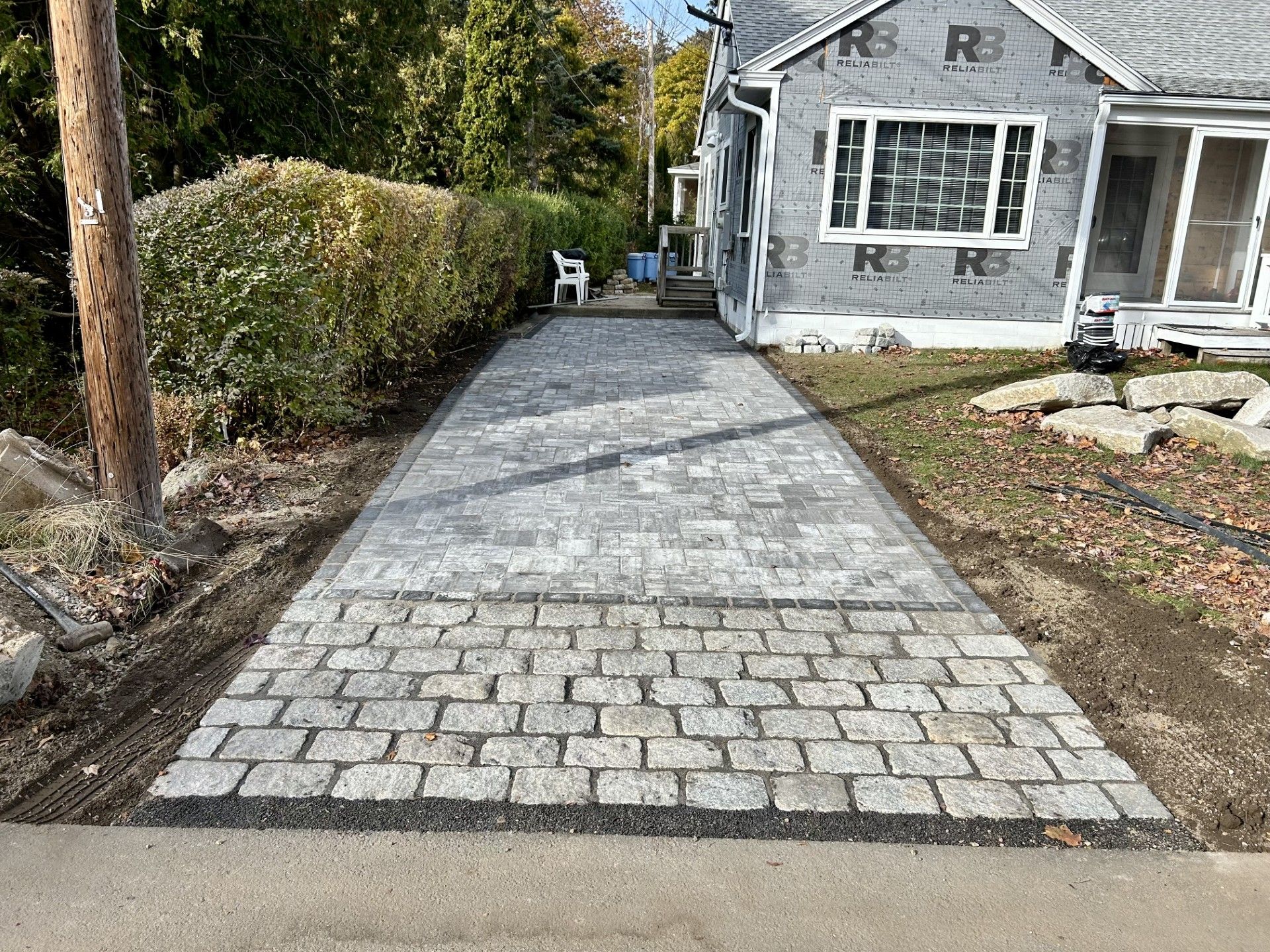 A new gray stone driveway leads to a house under renovation with unfinished exterior walls.