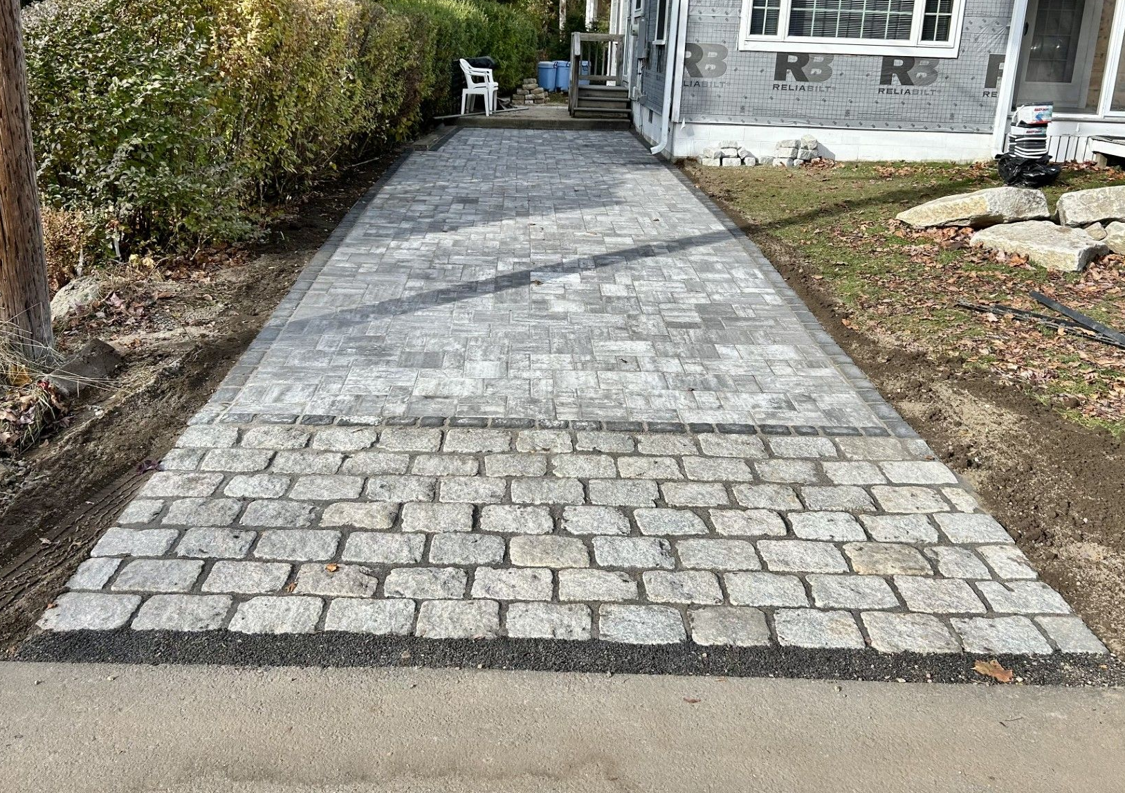 A new paver driveway featuring a textured stone apron leading to a grey patterned stone path beside a house.
