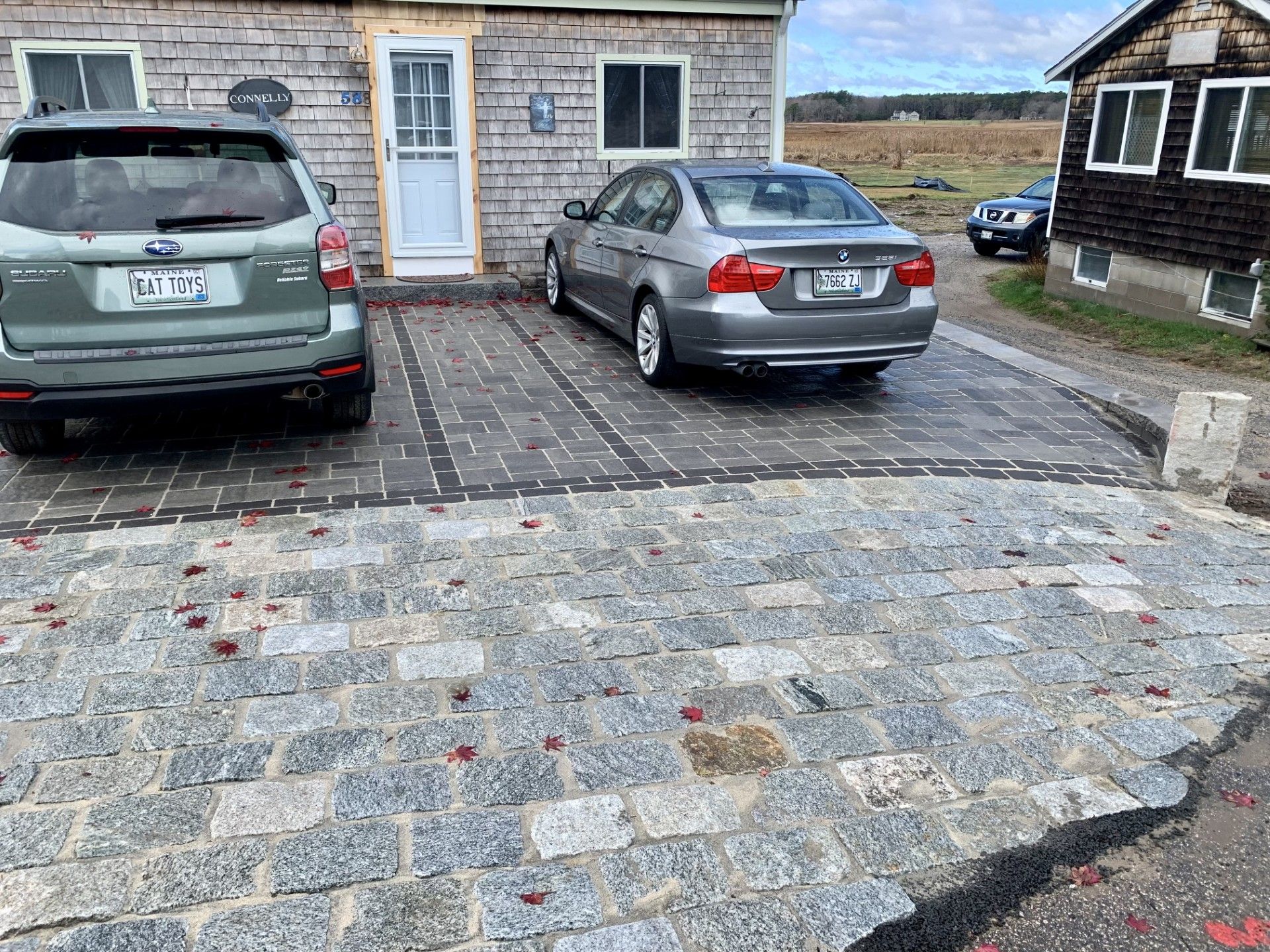 Two cars parked on a gray paved driveway in front of a rustic, wood-shingled building with a white door and windows.