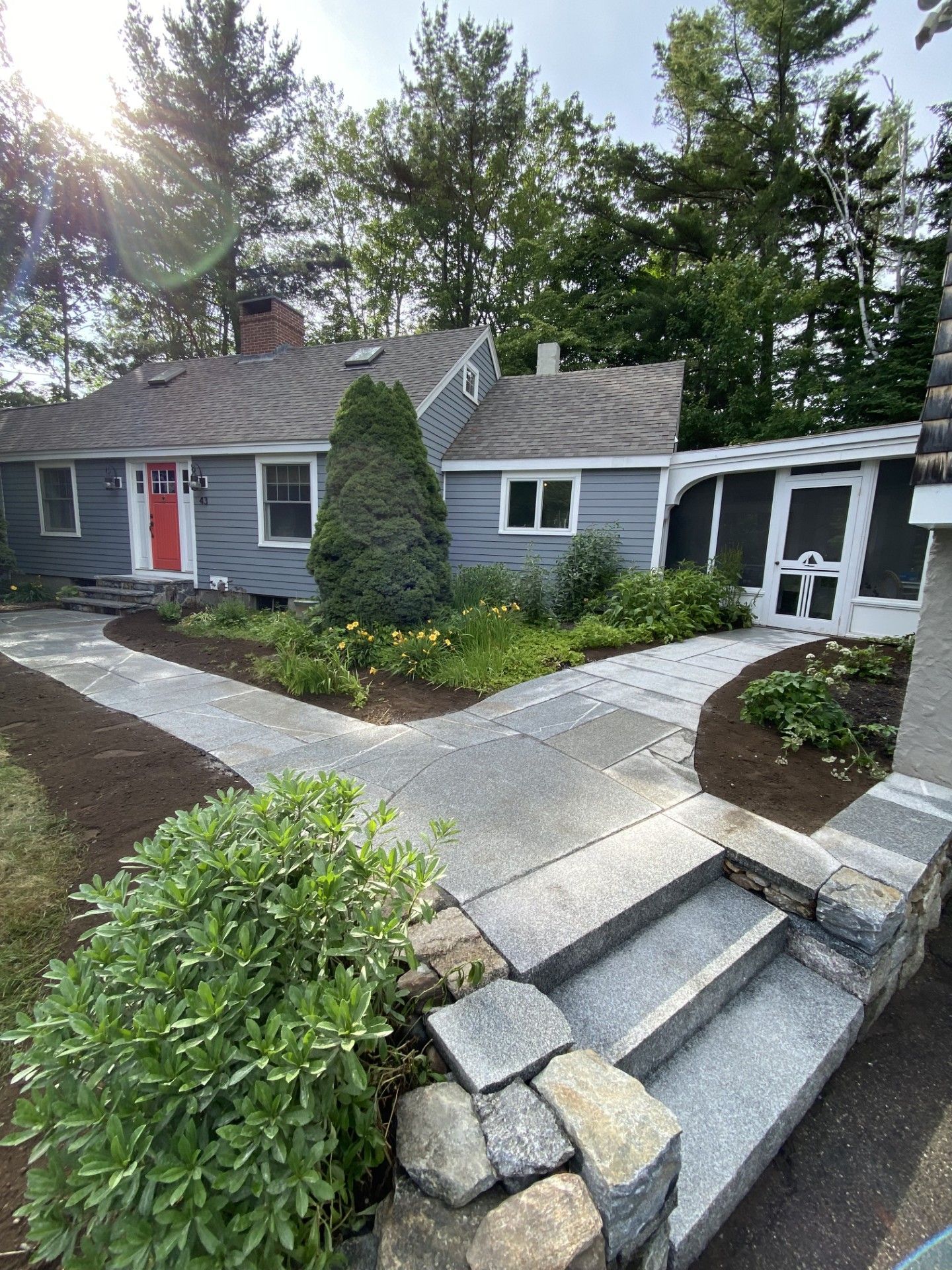 A gray cottage with a red front door, featuring a new stone walkway leading to stone steps and a white screened-in porch.