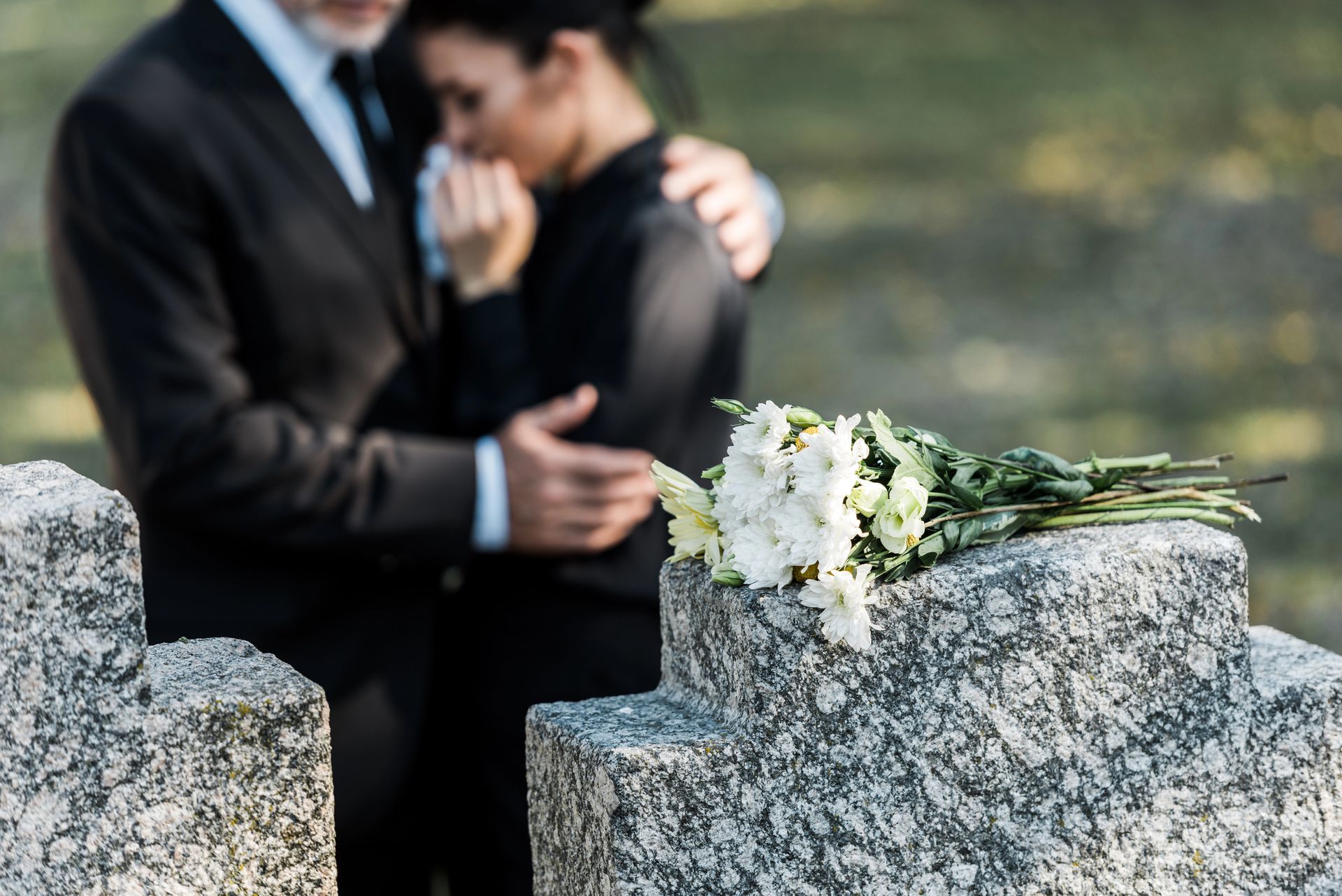Two suited hands gently holding fingers in front of a blurred outdoor background
