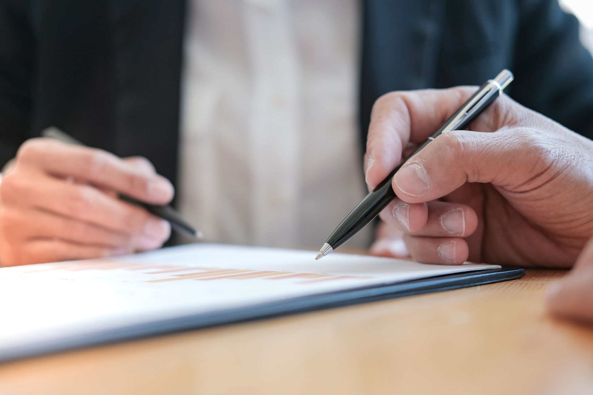 Hands signing a document with a pen at a table