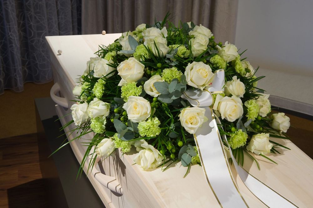 White rose and greenery funeral wreath on a white casket in a dim room