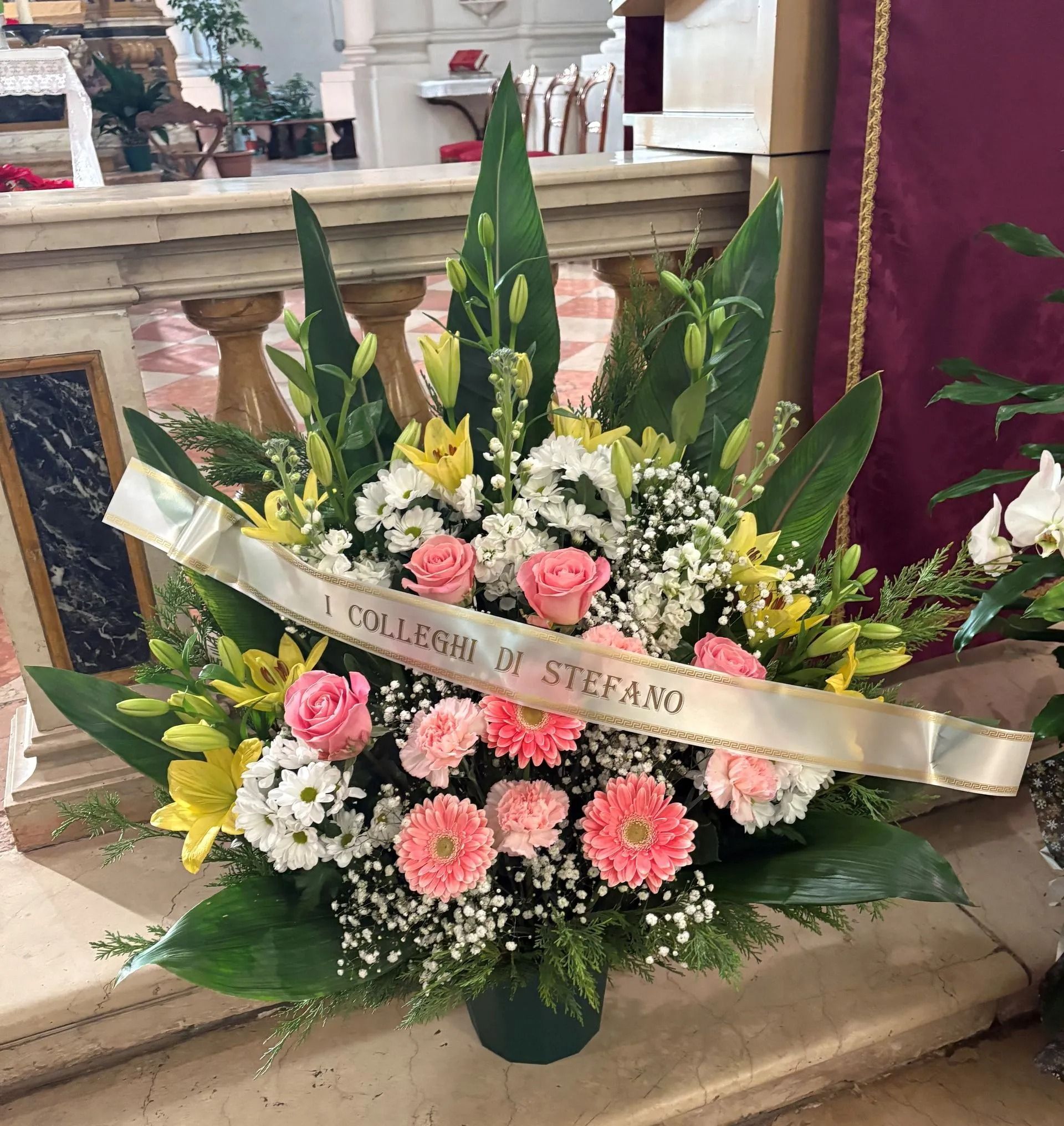 Floral funeral arrangement with pink, white, and yellow flowers and a ribbon reading “D. Stephen”