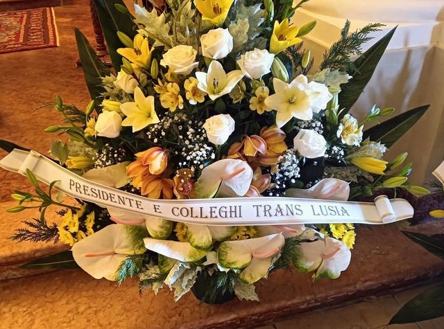 Floral arrangement with yellow and white flowers and a ribbon reading “Presidente Collegio Trans…”