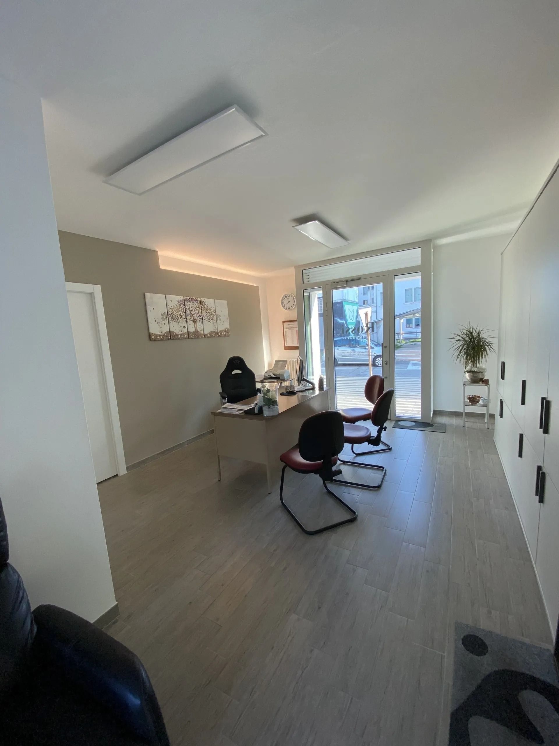 Modern office interior with desks, chairs, and a person working near large windows.