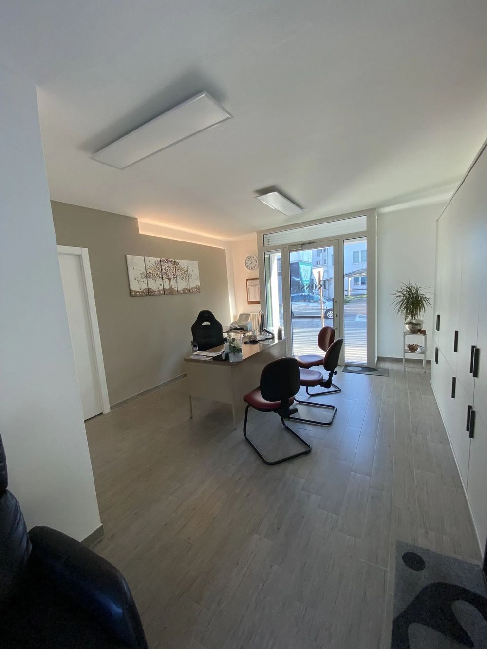 Modern office interior with desks, chairs, and a person working near large windows.